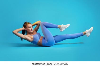 Fitness Workout. Sportswoman In Fitwear Doing Elbow To Knee Abs Crunch Exercising On Blue Studio Background. Athletic Female Flexing Abs Muscles Lying On Floor. Sport And Bodybuilding