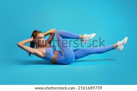Fitness Workout. Sportswoman In Fitwear Doing Elbow To Knee Abs Crunch Exercising On Blue Studio Background. Athletic Female Flexing Abs Muscles Lying On Floor. Sport And Bodybuilding