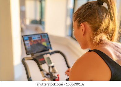 Fitness Workout Woman Training At Home On Smart Stationary Bike Equipment Connected Online Live Streaming Class Indoors For Biking Exercise. Indoor Cycling. Focus On The Sweat On Person's Back.