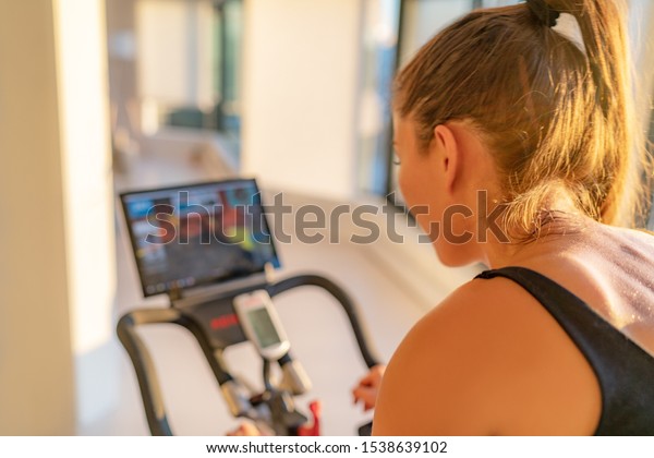 Fitness workout woman training at home on smart
stationary bike equipment connected online live streaming class
indoors for biking exercise. Indoor cycling. Focus on the sweat on
person's back.