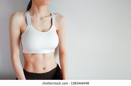 Fitness And Yoga Healthy Lifestyle Concept. Young Woman Wearing White Sport Bra And Pants With Muscular Body And Strong Six Pack Abs. Female Posing In Sportswear (Sports Clothes) On Gray Background.