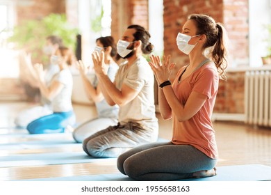 fitness, yoga and healthy lifestyle concept - group of people wearing face protective medical mask for protection from virus disease doing lotus seal gesture and meditating in seated pose at studio - Powered by Shutterstock