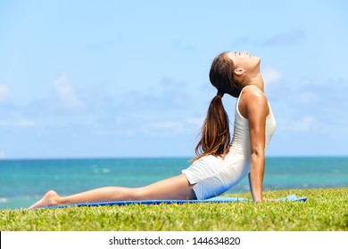 Fitness yoga woman stretching abdominal stomach muscles in cobra posture, bhujangasana. Fit fitness girl stretching out after exercising outside on beach in summer. Beautiful multiracial female model. - Powered by Shutterstock