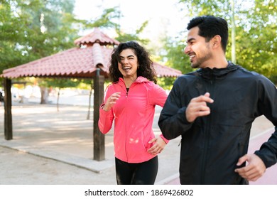 Fitness Young Woman And Young Man Talking And Flirting While Running In The Park. Latin Couple Smiling And Laughing While Working Out