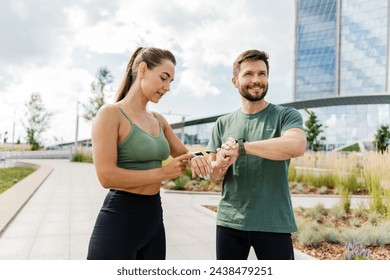 Fitness-focused couple syncing their smartwatches before a workout in an urban setting.

