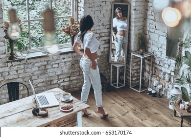 Fits Perfect. Full Length Rear View Of Attractive Young Woman Looking In The Mirror While Putting On Her Jeans