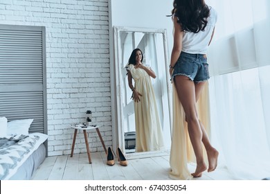 Fits Perfectly! Rear View Of Attractive Young Woman Trying On Her Dress While Looking In The Mirror At Home          