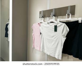 A fitting room with several casual clothing items, white t-shirt, a pink t-shirt, and a black skirt - Powered by Shutterstock