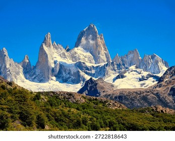 Fitz Roy mountain range rising above green vegetation in Patagonia.
