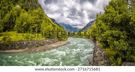 Fiume Dora Baltea (river) flows through a green valley with mountains and a cloudy sky in Aosta valley, Italy
