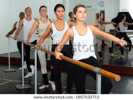 Five aduls people doing exercises on stretching ballet barre