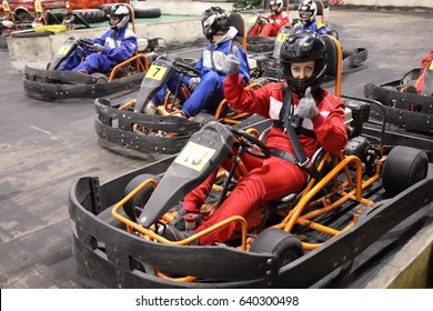 Five adults and one child in helmets prepares for driving karting, Woman in red thumbs up, focus on right woman