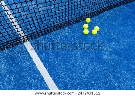 five balls next to the net of a blue paddle tennis court