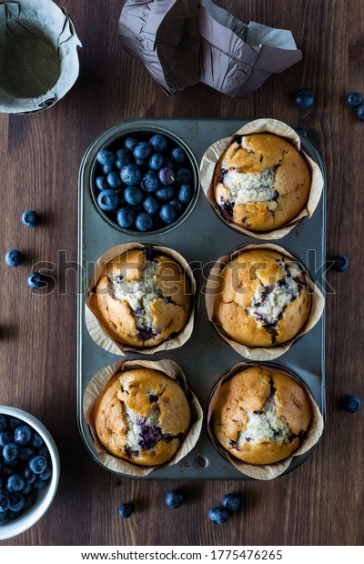 Five blueberry muffins in a muffin tin with\
one cup filled with\
blueberries.