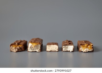 Five broken chocolate bars with different visible fillings isolated on a gray background, showcasing confectionery variety, textures, and product selection concepts