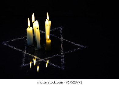 Five burning candles and the Star of David against a black background.
