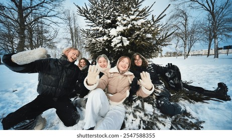 Five cheerful schoolgirls waving at camera, posing by snowy fir tree in winter park, enjoying winter holidays - Powered by Shutterstock