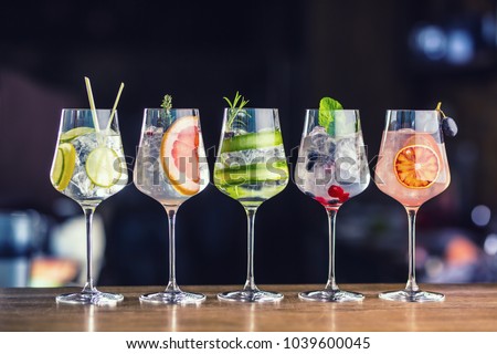 Five colorful gin tonic cocktails in wine glasses on bar counter in pup or restaurant. 