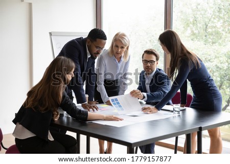 Five diverse focused employees make project research at group meeting. Expressing professional opinion, offering solution, working on analysis, reviewing statistics financial data do paperwork concept