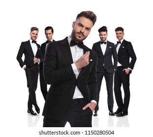 Five Elegant Groomsmen Standing On White Background, Dressed In Black Tuxedoes,with Arrogant Leader In Front