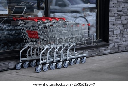 five empty shopping carts put together outside of grocery store stainless steel or metal with wheels and red handles stacked together outside of grocery store window horizontal format room for type 