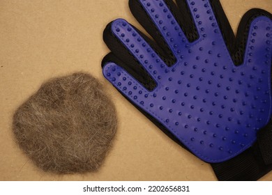 Five Finger Deshedding Glove And A Ball Of Cat Hair On A Light Brown Background