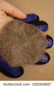 Five Finger Deshedding Glove And A Ball Of Cat Hair On A Light Brown Background