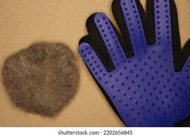 Five Finger Deshedding Glove And A Ball Of Cat Hair On A Light Brown Background