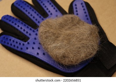 Five Finger Deshedding Glove And A Ball Of Cat Hair On A Light Brown Background