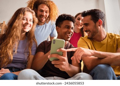 Five friends laughing and joking while looking at their phone at home.
