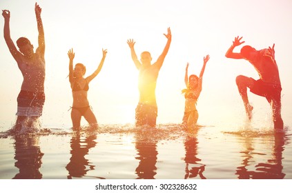 five friends making party at sunrise. boys and girls jumping and dancing in the ocean