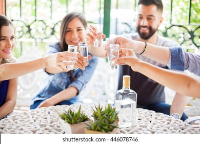Five friends raising their glasses and making a toast with tequila shots during a party outdoors