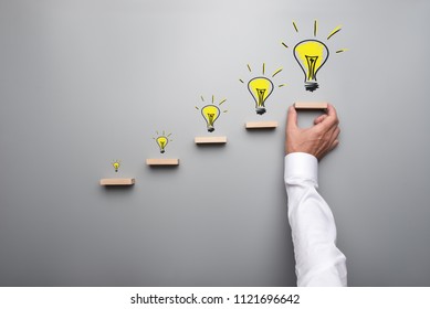 Five hand drawn light bulbs representing a new idea on wooden steps with male hand holding or placing the last step. Conceptual image of business vision.