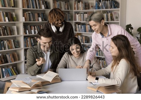Five happy multiracial students, groupmates look at laptop screen, discuss online task, make presentation, work on joint on-line project met in library for doing collaborative exercise use modern tech