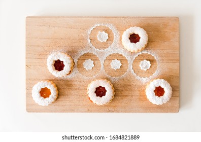 Five homemade linzer cookies are chilling on a cutting board.