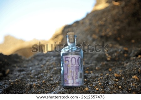 Five hundred euros, currency of the European Union. Image illustrating money laundering. Bottle with a 500 euro bill inside found by the sea, silhouetted against a dark sandstone rock background.