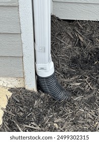 Five inch gutter drain reduced down to four inch corrugated pipe running through bed of mulch.