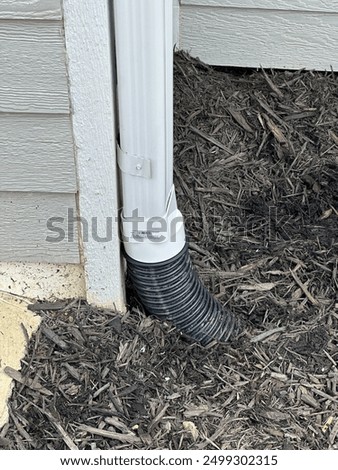 Five inch gutter drain reduced down to four inch corrugated pipe running through bed of mulch.