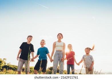 Five kids brothers and sisters teenagers and little kids walking on the green grass meadow with evening sunset background light holding hands in hands and smiling. Happy and careless childhood concept - Shutterstock ID 2162911761