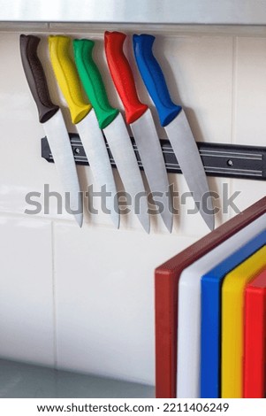 Five kitchen knives with colorful handles hang on a magnetic holder. Multicolored kitchen cutting boards. Professional kitchen equipment for chefs.Food safety. HACCP. Place for text
