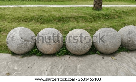 Five large, grey stone spheres rest a concrete path, nestled vibrant green grass.