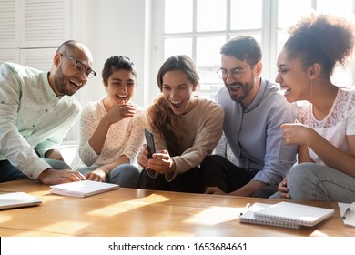 Five laughing attractive multi-ethnic friends having fun indoors using smart phone new cool free application, making video call chatting with mates, photographing or vloggers recording video concept - Powered by Shutterstock