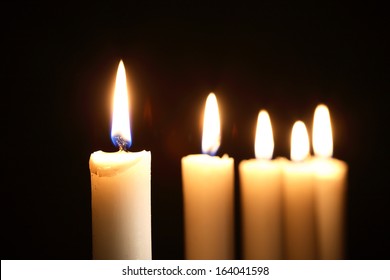 Five lighting candles in a row on dark background