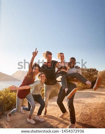 Five millennial friends on a road trip have fun posing for photos on a coastal path, full length