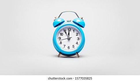 Five Minutes To Twelve. Close-up Photo Of A Turquoise Alarm Clock With A Black And White Clock Face, Placed On A White Background.	