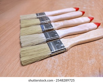 Five paintbrushes with red-tipped wooden handles arranged in a row on a wooden surface - Powered by Shutterstock