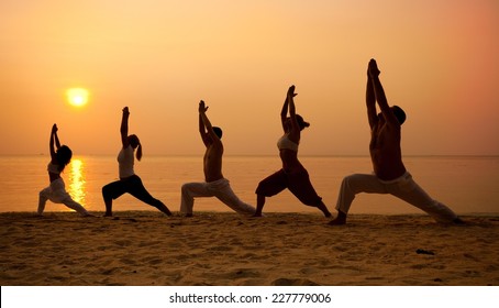 Five people practising yoga at the beach - warrior I pose. - Powered by Shutterstock