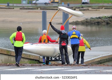 A five person team prepares to launch their scull boat with a long float into the waters/Launching a Scull Boat with Float/A team launches their scull boat with a long float into the waters.  - Powered by Shutterstock