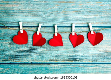 Five red hearts on wooden pegs on a rope on a blue wooden background, Valentines Day theme. Free space for text