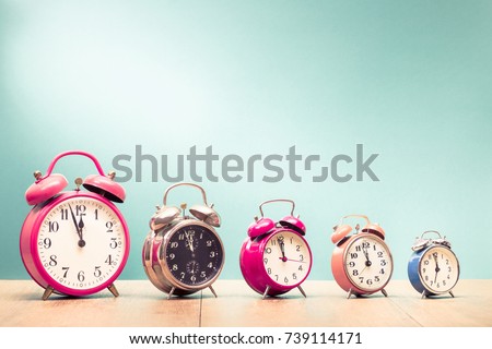 Five retro alarm clocks with last minutes to twelve o'clock on wooden table front gradient mint green wall background. Vintage old style filtered photo